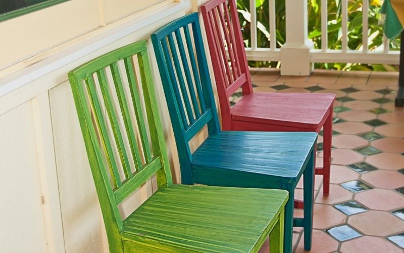 Photo of three chairs with green, blue and red colors that may attract birds coming to the porch
