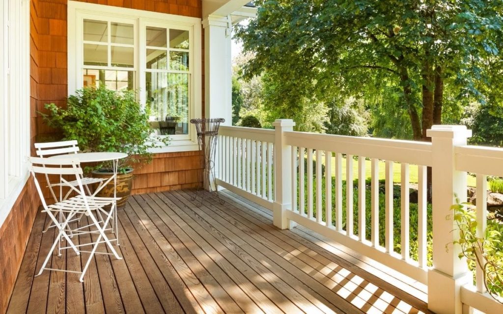 A clean porch with white railings, a plant in large pot and a tree nearby with no birds pooping.
